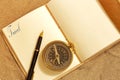 Leather journal, with the word travel on a page, with a fountain pen and antique compass in sand. Royalty Free Stock Photo