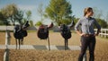 Leather Saddles Hanging On The Wooden Fence In The Sandy Arena - Girl Posing Royalty Free Stock Photo