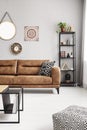 Leather sofa with black and white pillow in real photo of sitting room interior with metal rack with books, decor and fresh plant