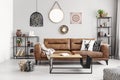 Leather sofa with pillows and blanket in elegant living room interior with metal shelves and modern coffee table,