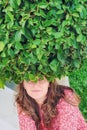 The leaves of the round crown of the bush create a hairstyle effect. Woman sits under a round tree shrub