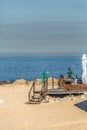 View of technological senior woman taking sunbath and using her mobile phone on beach club, sea as background, in Portugal