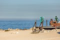 View of technological senior woman taking sunbath and using her mobile phone on beach club, sea as background, in Portugal