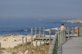 View of woman seat on wood bench in pedestrian wooden walkway, beach and sea as