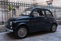 Black Fiat vintage cinquecento 500 car parked in front of railings outside church in Puglia, Southern Italy.