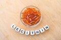 Lecithin gel pills in a round glass bowl and with the word Lecetin from the letters of cubes on a light wooden background. Soy