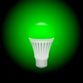 LED green economical light bulb glowing on a dark background.