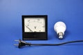 LED lamp and black analog voltmeter and a black wire on a blue background.