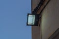 An LED lantern mounted on the street wall dimly illuminates the wall during dusk on dark blue sky background. The