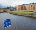 Riverside view of leeds near the dock entrance with sign next to the canal and waterside apartments with the minster and city