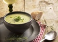 Leek cream soup in a dark bowl on a plate, wine, bread and spoon