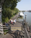 Man on bench and tourists passing on harbor embankment in centre of old german town of leer on sunny summer day