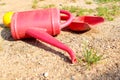 Left children toys on the sand. Red watering can, shovel and yellow ball.