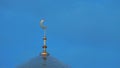 The top of the golden minaret of the mosque with a crescent is a symbol of Islam against a blue sky with clouds. Left on the frame