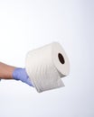 Left hand in blue glove holding with thumb a roll of toilet paper Royalty Free Stock Photo