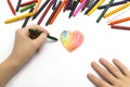 Left hand drawing a heart shape with colored crayons pastels