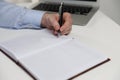 Left-handed man writing in notebook at white table, closeup Royalty Free Stock Photo