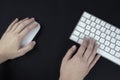 Left-handed woman holds a computer mouse in her left hand. White and silver keyboard on black background Royalty Free Stock Photo