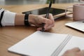 Left-handed woman writing in notebook at wooden table, closeup Royalty Free Stock Photo