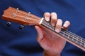 Left musician hand clamps the chord on the ukulele, side view