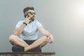 In left part of image young attractive bearded hipster man in sunglasses and white T-shirt is sitting cross-legged Royalty Free Stock Photo