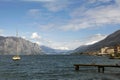 On the left, a sailing yacht sails along the sea bay between the mountains. On the right is a wooden pier on which wild ducks walk