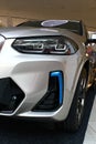 Left side detail of front mask and headlights of battery electric compact luxury crossover SUV BMW iX3. silver metallic colour