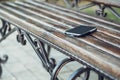 Left smartphone on a wooden bench in urban public park. Lost and forgotten personal thing outdoors in the city