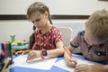 Lefty girl and righty boy writing at same desk and nudge each other with elbows, left-hander day