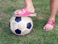 Leg of Asian little girl wear pink sandal stand on soccer ball on green grass field Royalty Free Stock Photo