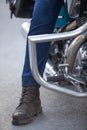 Leg of biker with leather motorcycle boot stepping on asphalt road, person sitting on motorbike, close-up view