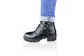 Leg in blue rolled up jeans and black lace-up boot with buckles and straps, isolated on white.