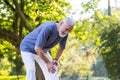 Leg injury during walking and sports training. Senior gray-haired man standing bent over in the park and holding his Royalty Free Stock Photo