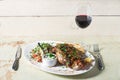 Leg of lamb baked with sauce in the white plate closeup with a side dish of rice. Rustic wooden table and a glass of red Royalty Free Stock Photo
