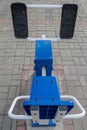 Leg workout exercise machine with plastic blue seat, metal white handrails and black stand pads for feet attached with rivets.