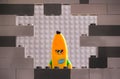 Lego Banana Guy minifigure looking through a hole in gray wall with gray background