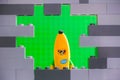 Lego Banana Guy minifigure looking through a hole in gray wall with green background