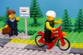 Lego boy riding bicycle waving to woman with suitcase