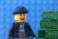 A Lego burglar minifigure standing near a pile of money against a blue baseplate background