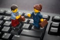 Lego businessman and businesswoman minifigures standing on a black computer keyboard