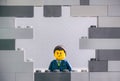 Lego businessman minifigure looking through a hole in gray wall