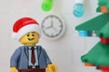 A Lego businessman minifigure wearing a Santa hat and standing next to a Christmas tree in his office
