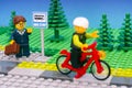 Lego busineswoman with suitcase standing at bus stop and waving to boy riding bicycle