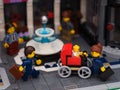 A Lego city square with businessperson minifigures. A Lego businesswoman pushing a stroller with a baby minifigure in it