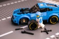 Lego driver minifigure fixing wheel of Chevrolet Camaro ZL1 race car by LEGO Speed Champions. Road baseplate background