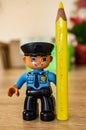 Lego Duplo police officer holding a yellow pencil.