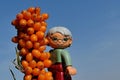 LEGO Duplo toy figure of elder lady with spectacles and grey hair standing next to dense cluster of orange Sea Buckthorn