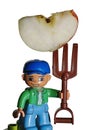 LEGO Duplo toy figure of farmer boy in blue baseball cap holding large slice of apple