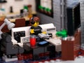 A Lego gamer minifigure playing video games using a controller on a flatscreen tv at home. A soda can and a cell phone on the