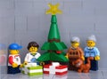 A Lego grandparents, grandchildren and cat minifigures standing near a Christmas tree that has a presents under it